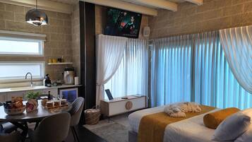 A hotel room with a bed, a desk with a computer, a window with curtains, and a television on the wall.