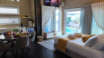 Habitación de hotel moderna con cama, zona de comedor, televisor y vista a una piscina.
