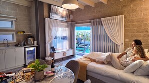 A modern hotel room with a sofa, a dining table with a plant, a laptop, and a view of a swimming pool. - Ahuzat Maya (Ma'ale Yosef)