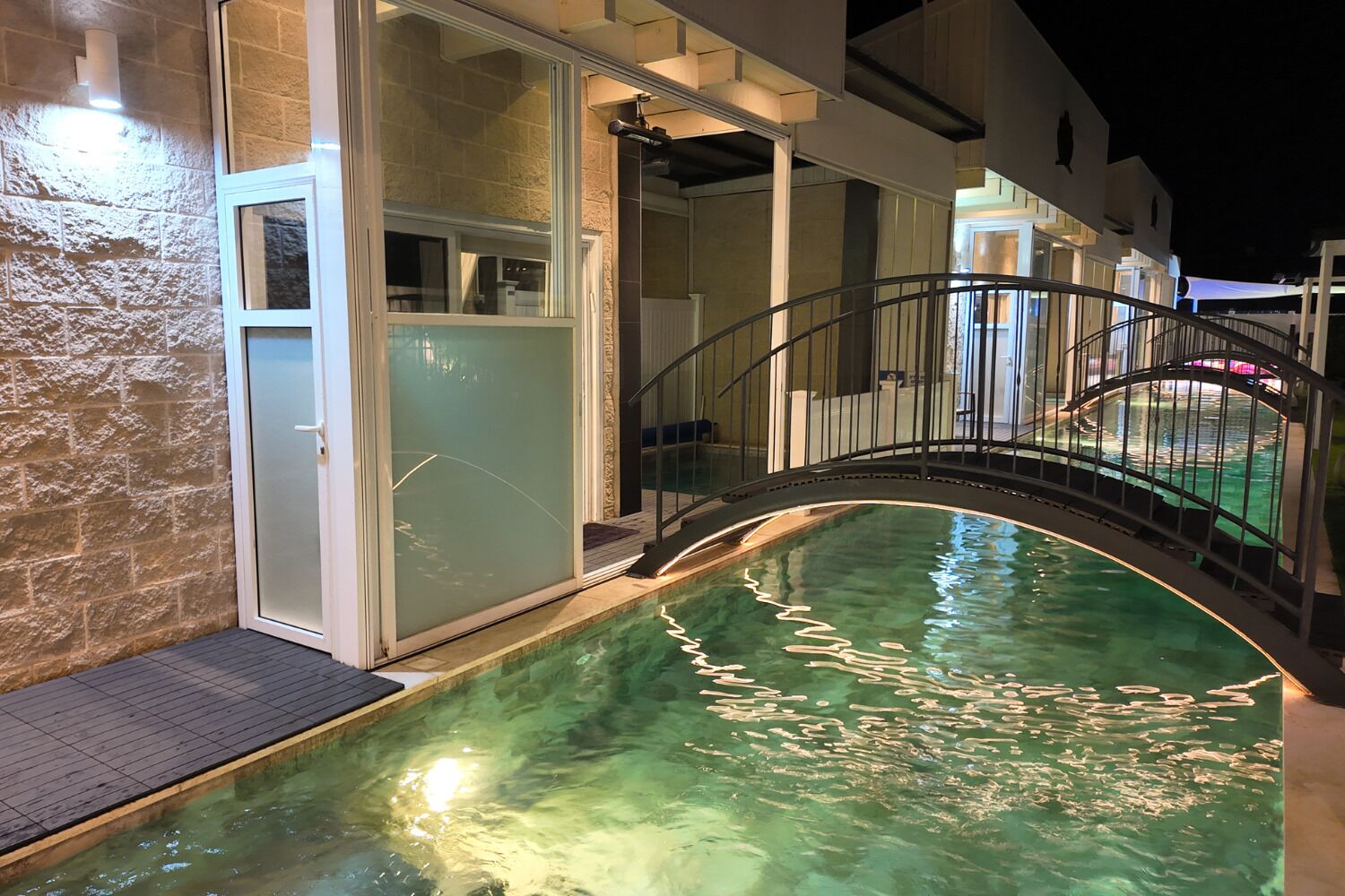 An indoor swimming pool with a glass wall, a metal staircase, and a stone wall.