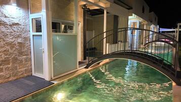 An indoor swimming pool with a glass wall, a metal staircase, and a stone wall.