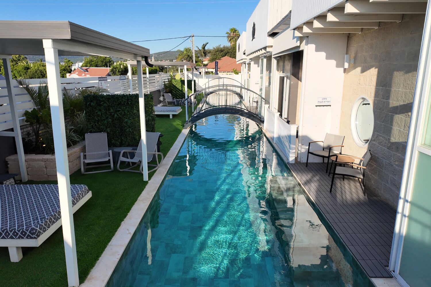 Una piscina con un puente, rodeada de asientos al aire libre y una zona cubierta.