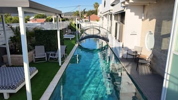 Una piscina con un puente, rodeada de asientos al aire libre y una zona cubierta.