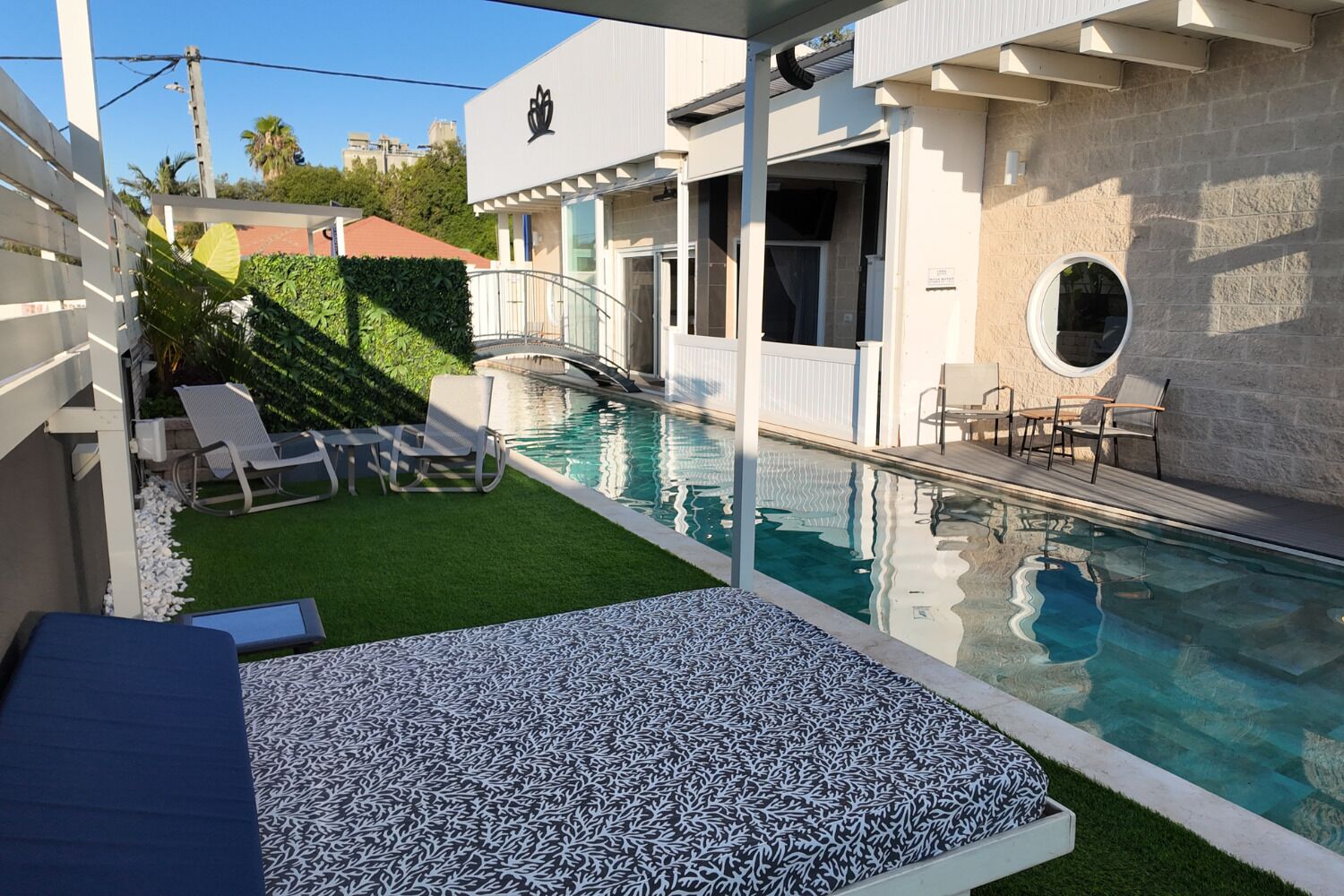 Una piscina con un pequeño solárium, sillas de descanso y un área de estar cubierta.