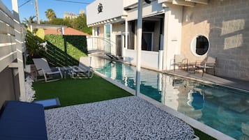 Una piscina con un pequeño solárium, sillas de descanso y un área de estar cubierta.