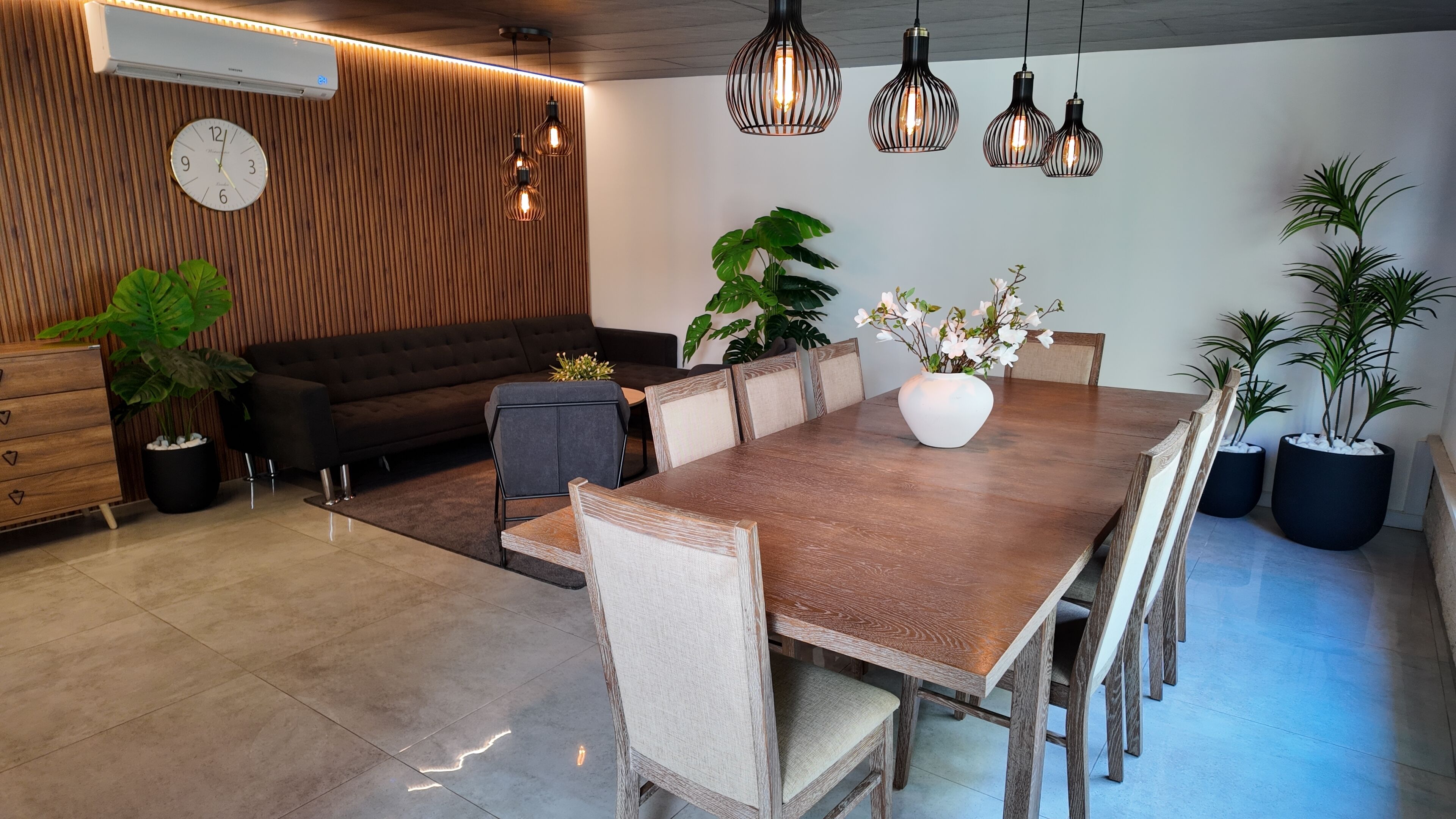 Uma área de refeições moderna com uma mesa de madeira, cadeiras e luminárias pendentes.