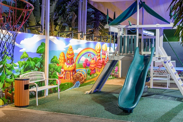 Ein Spielplatz mit Rutsche, Kletterbereich und einer Bank.