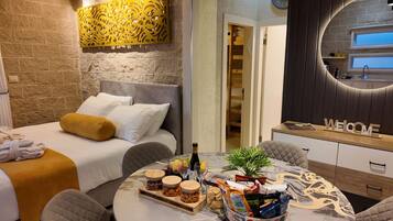 Een hotelkamer met een bed, nachtkastje met snacks, een ronde tafel met een plant en een welkomstbord.