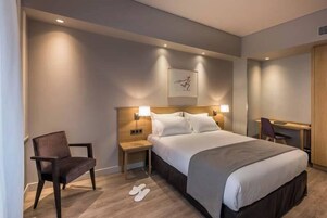 Une chambre d’hôtel avec un grand lit, une chaise, un bureau et une œuvre d’art accrochée au mur.