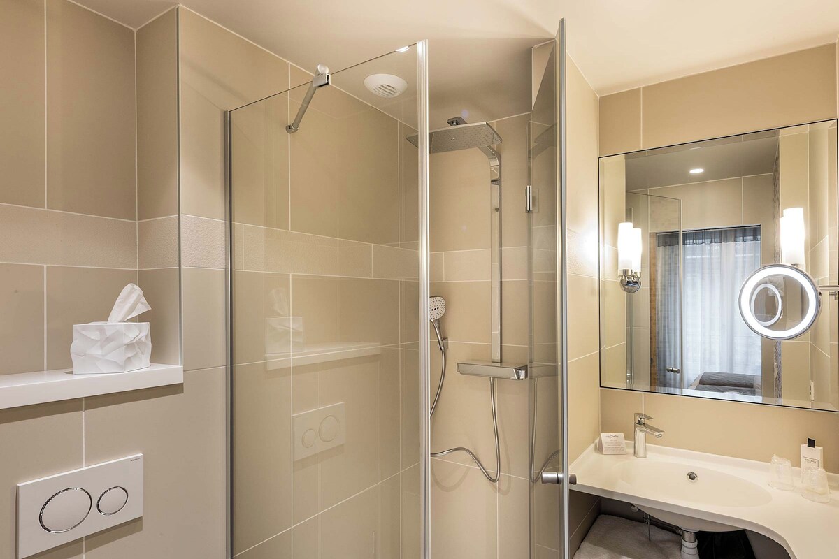 A modern bathroom with a glass-enclosed shower, a vanity with a mirror, and a towel rack.