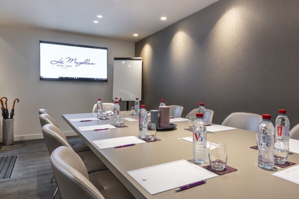 A conference room with a long table, chairs, water bottles, and a projector screen displaying "Le Magellan HOTEL PARIS".