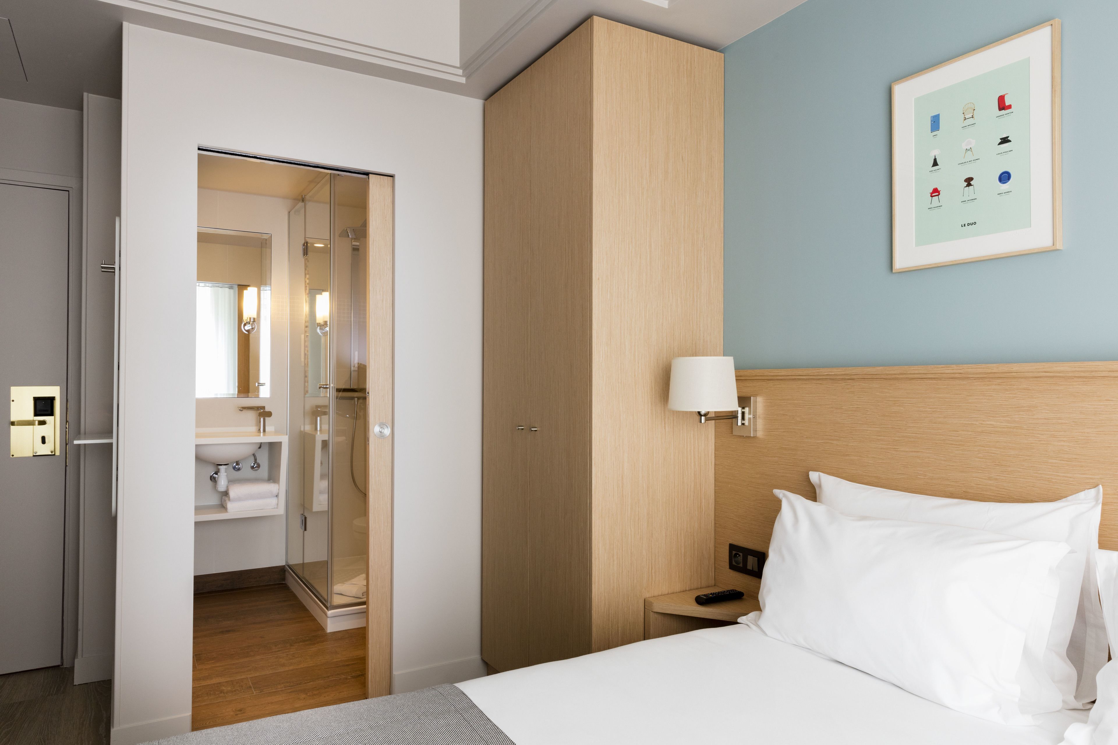 A hotel room with a bed, a nightstand, a bedside lamp, a wardrobe, and a framed picture on the wall.