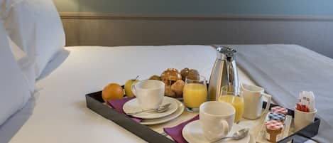 Bandeja de desayuno con tazas, un jarro de jugo de naranja y pasteles sobre una cama.