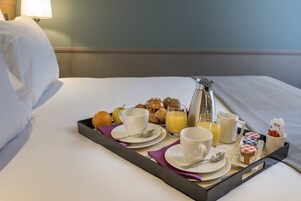 Un plateau de petit-déjeuner avec des tasses, un pichet de jus d’orange et des viennoiseries, le tout posé sur un lit.