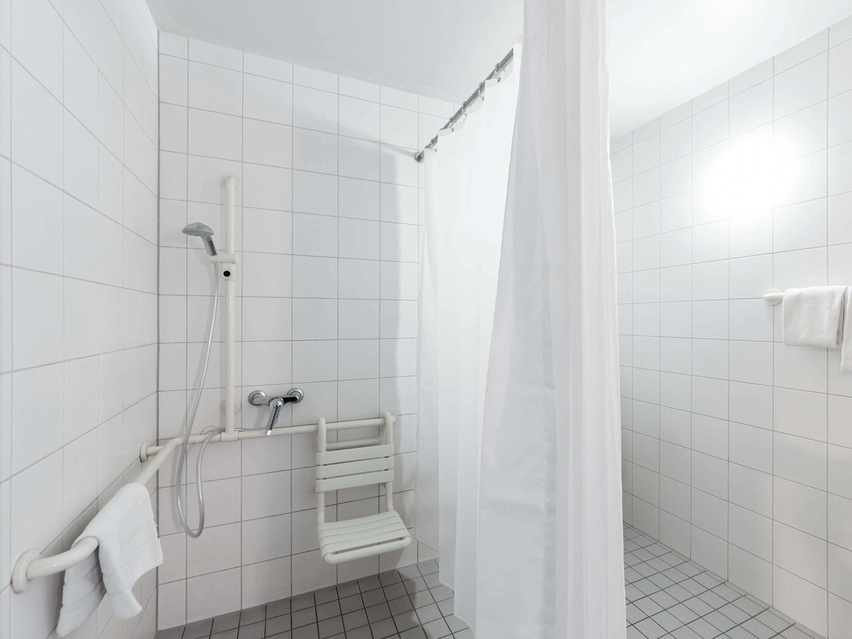 A modern shower area with white tiles, a glass shower enclosure, and a white towel rack.