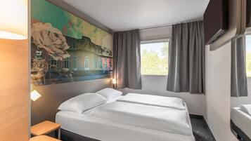 Habitación de hotel con cama, escritorio, ventana con cortinas, televisor montado en la pared y un cuadro.