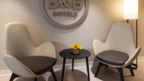 Cartel de un hotel B&B, dos sillones, una mesita con un florero y una lámpara de pie.