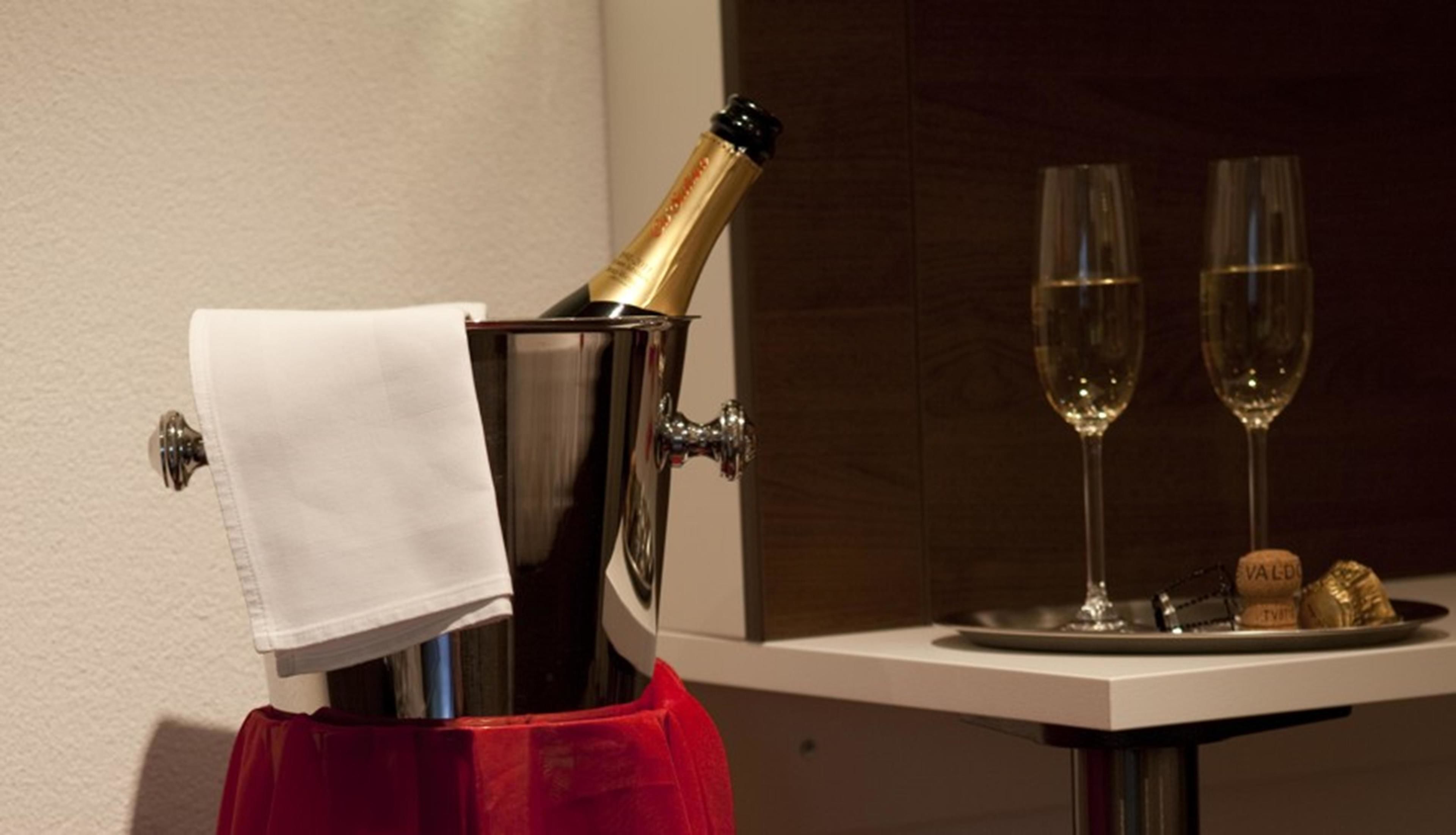 Een minibar met een champagnefles, twee glazen en een kurkentrekker op een dienblad.