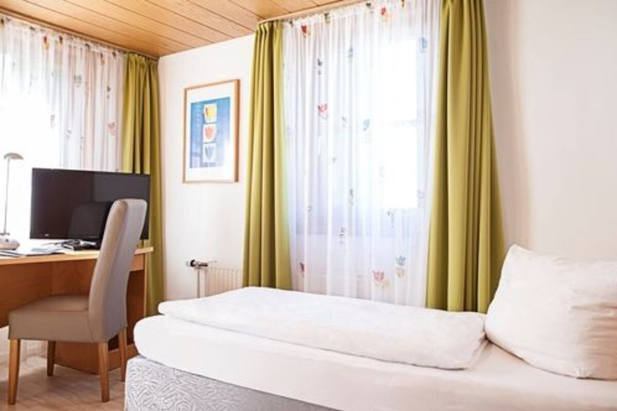 A bedroom with a bed, a desk with a computer, and a chair.