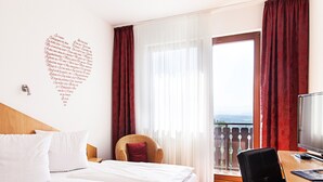A hotel room with a bed, a desk with a computer, a chair, and a balcony with a view. - Hotel Restaurant Kaiser (Herrenberg)