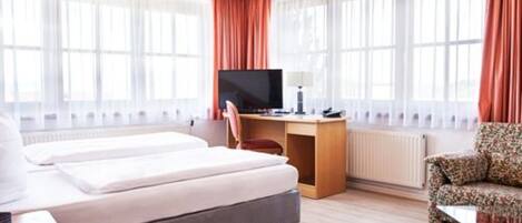 A hotel room with a bed, a desk with a computer, a chair, and a sofa.
