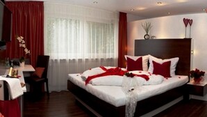 A modern hotel room with a large bed, red curtains, a bedside table, and a nightstand with a vase of flowers. - Hotel Restaurant Kaiser (Herrenberg)