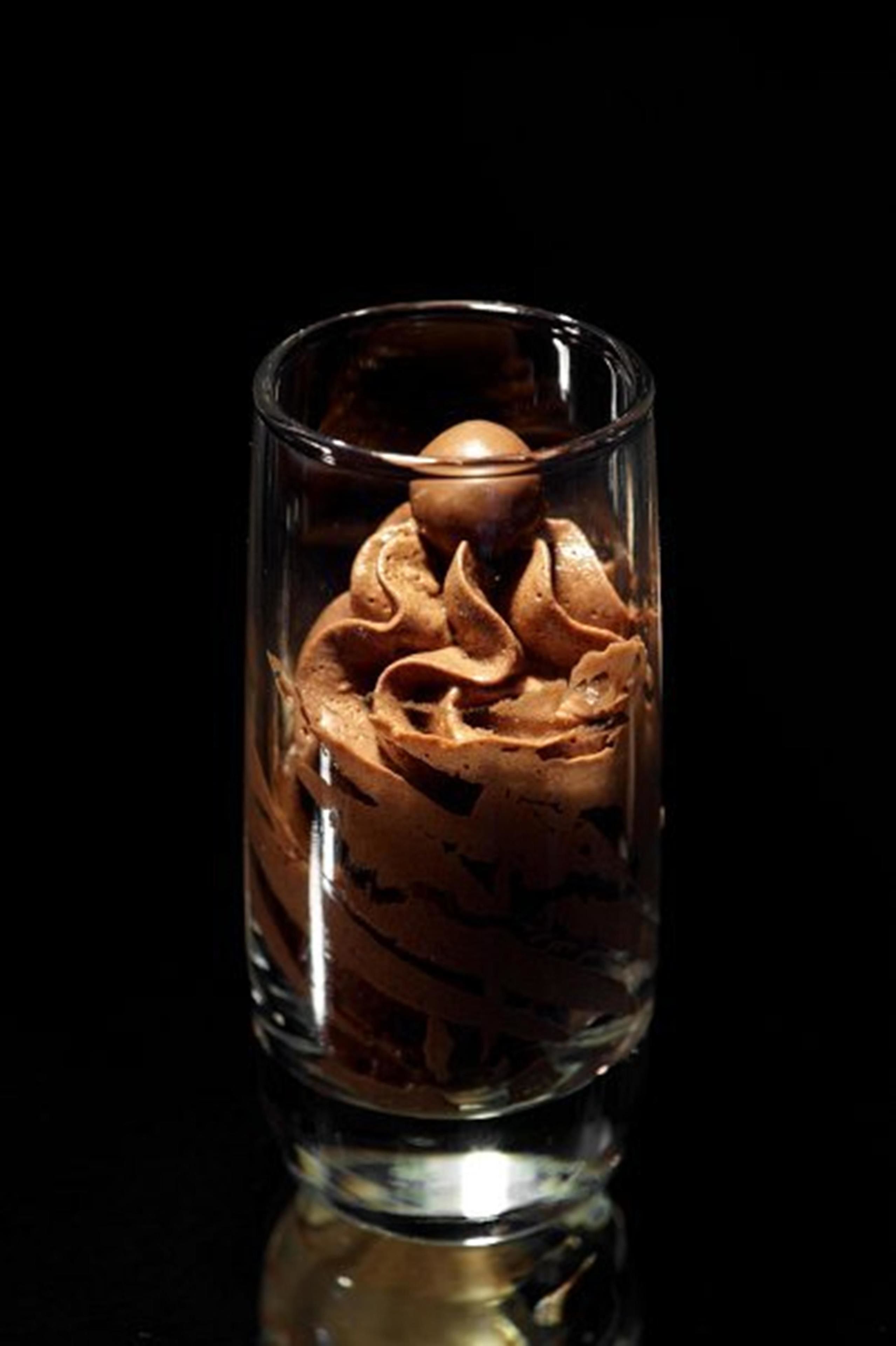 Un verre contenant un dessert à plusieurs couches, peut-être une mousse au chocolat, sur un fond sombre.