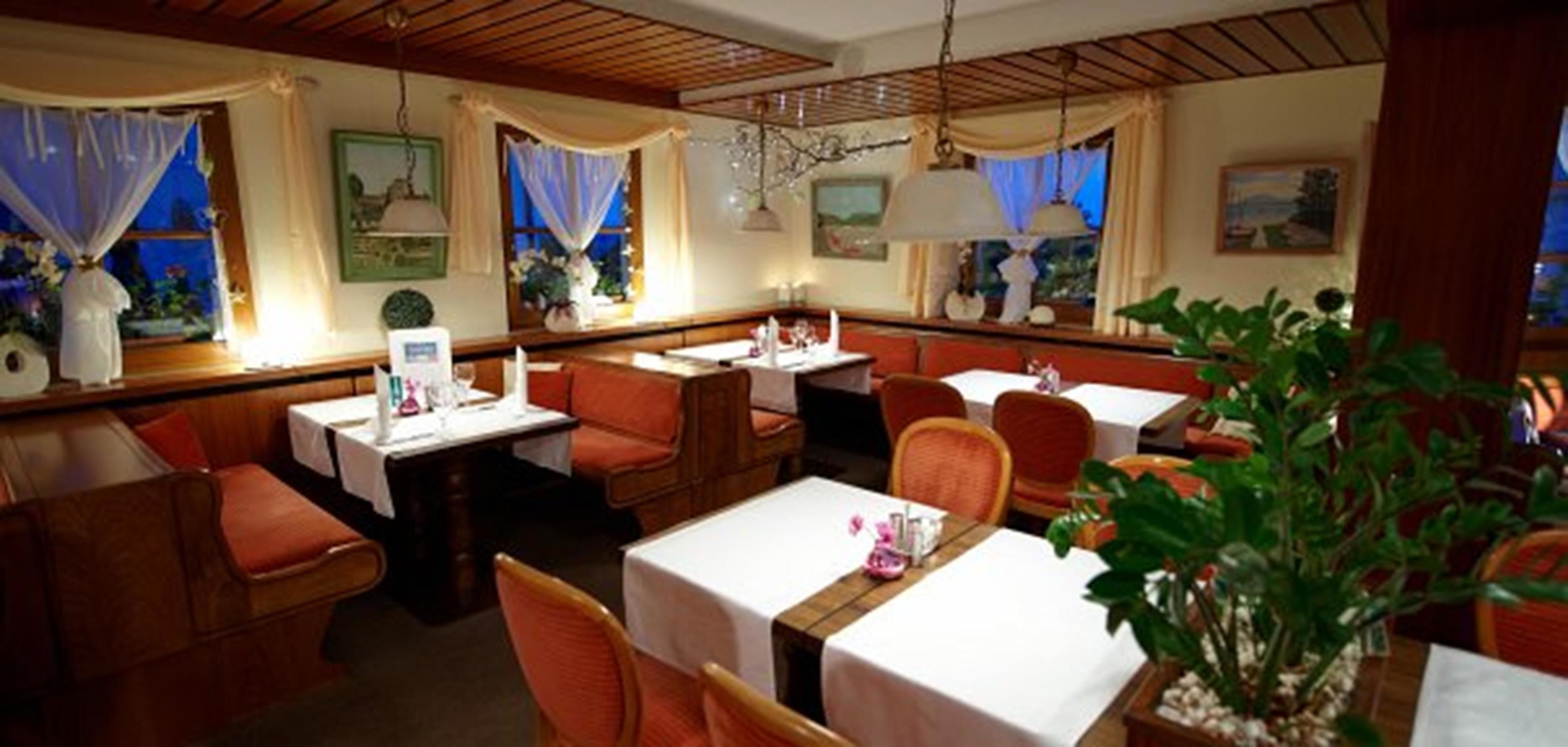 Un restaurant amb seients a boxes i taules, sostre de fusta i plantes decoratives.