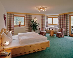 A bedroom with a wooden bed, a small table, two chairs, a potted plant, and plaid curtains.