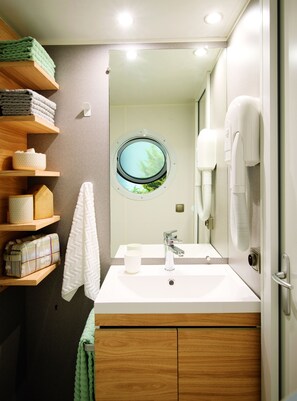 A bathroom with a wooden vanity, a round window, a towel rack, and a hairdryer.