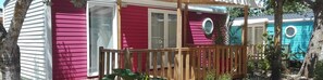 A row of colorful mobile homes with a wooden deck and a glass door.