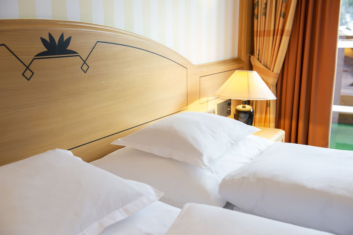 A hotel room with a wooden headboard, white bedding, and a lamp on a bedside table.