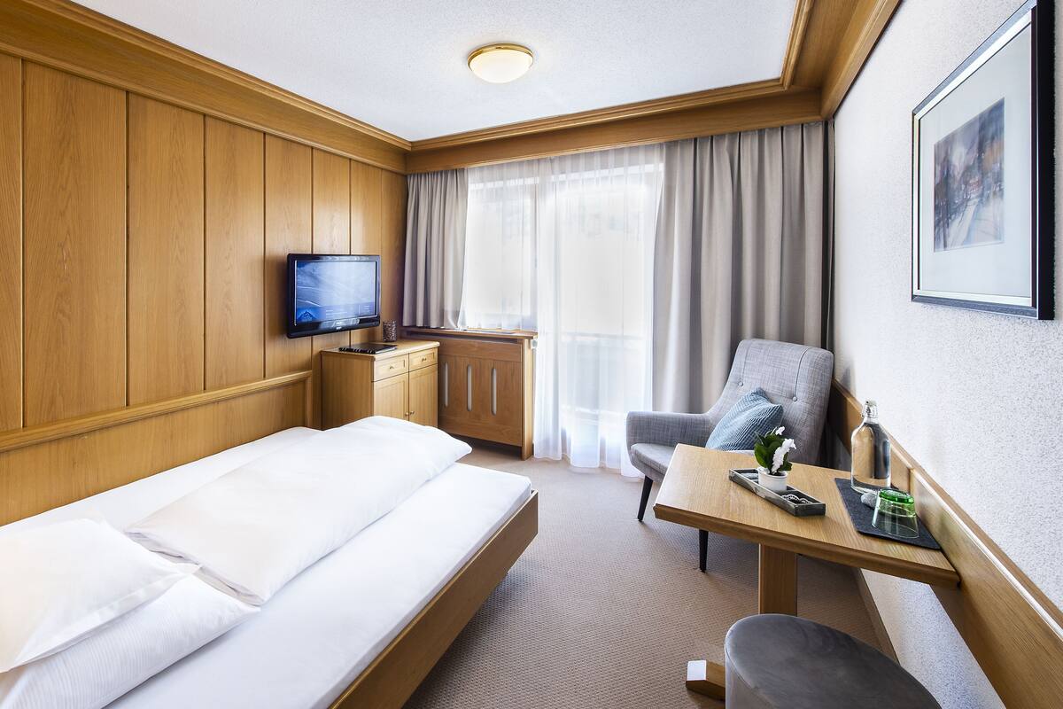 A hotel room with a bed, a desk, a chair, a TV, and a window with curtains.