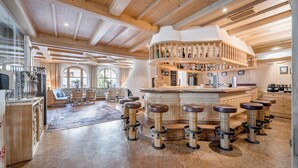 A spacious bar area with a curved counter, multiple stools, and a variety of bottles. - Hotel Rössle (Galtur)