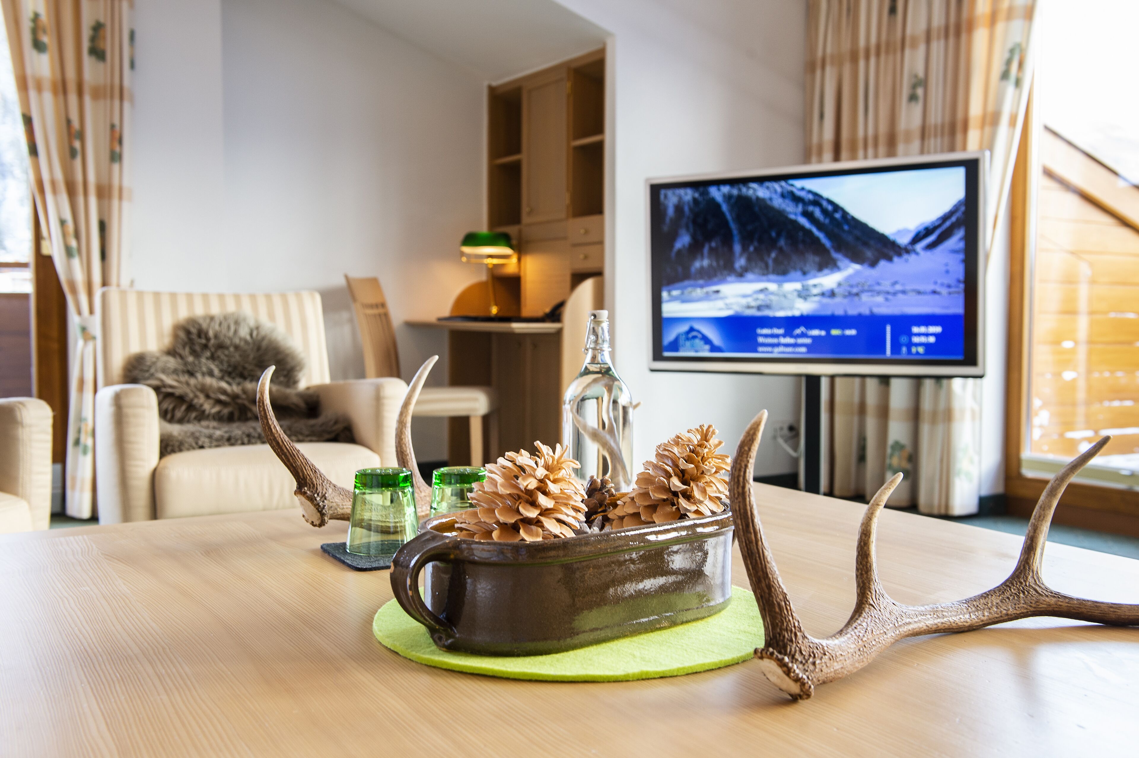 A living room with a wooden table, a sofa, and a television displaying a snowy landscape.