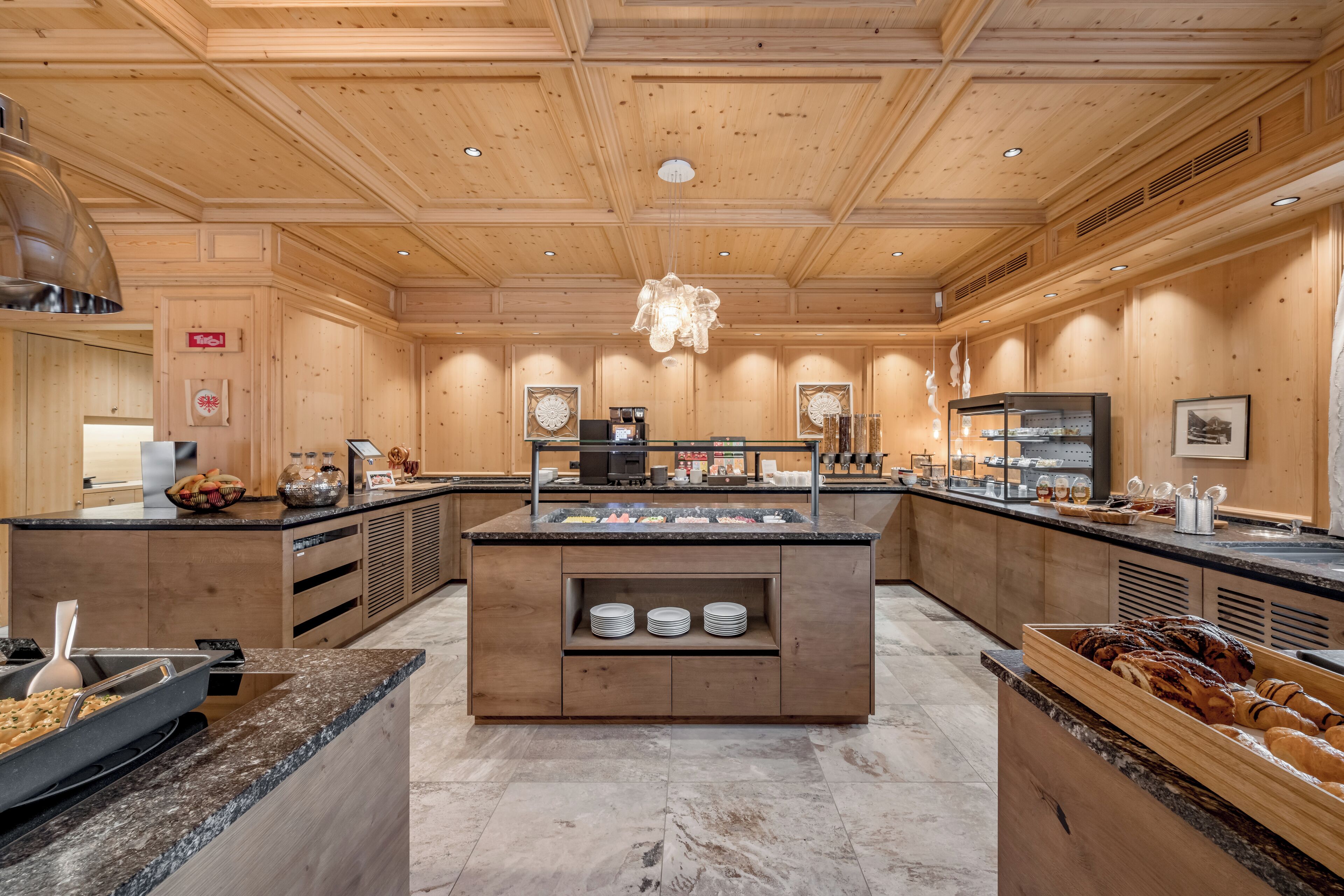 Une cuisine spacieuse avec un revêtement mural en bois, des plans de travail en granit et un îlot central doté d’une machine à café et d’un présentoir pour les aliments.