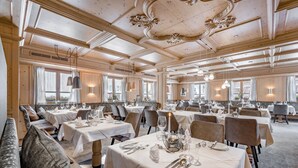 A spacious dining area with multiple tables set for dining, elegant chandeliers, and large windows allowing natural light. - Hotel Rössle (Galtur)