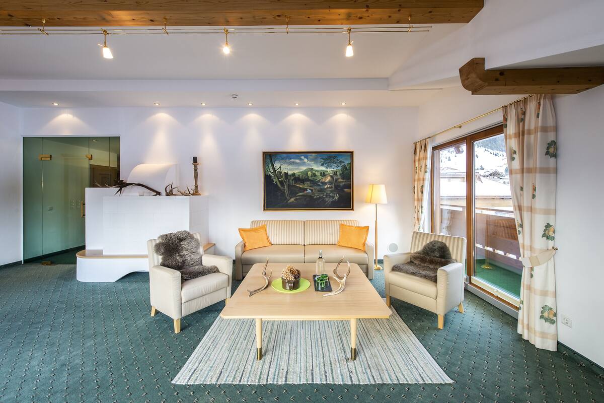 A cozy living room with a sofa, two armchairs, a coffee table with antlers, a painting, and a window with curtains.