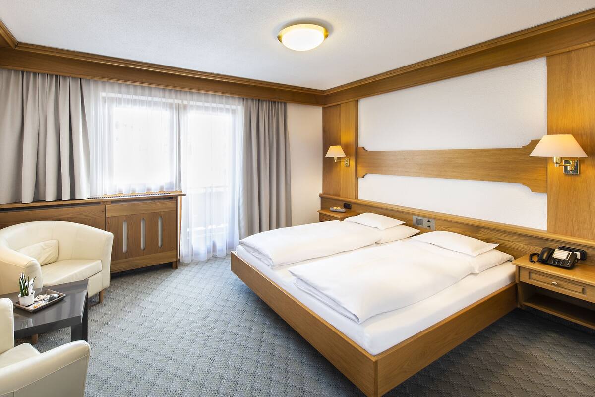 A hotel room with a large bed, a desk, a chair, and a window with curtains.