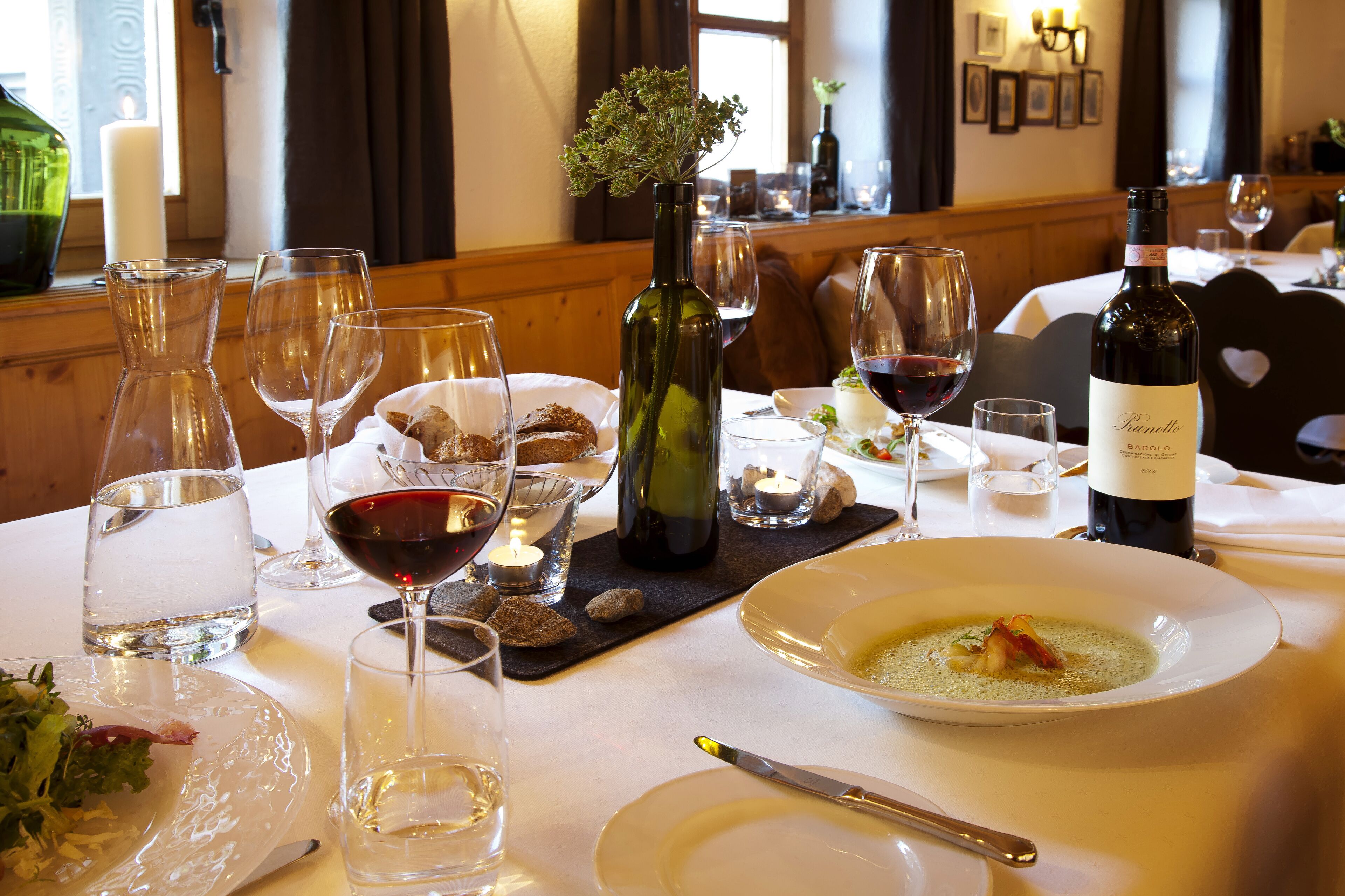 Une table à manger dressée avec des verres à vin, une bouteille de vin et une assiette de soupe.