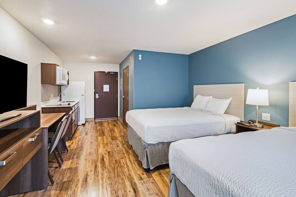 Una habitación de hotel con piso de madera, una cama con ropa de cama blanca, un escritorio con una silla y un televisor.