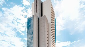 Een modern hotel met een glazen gevel, een opvallend bord en een klassiek pand ernaast.