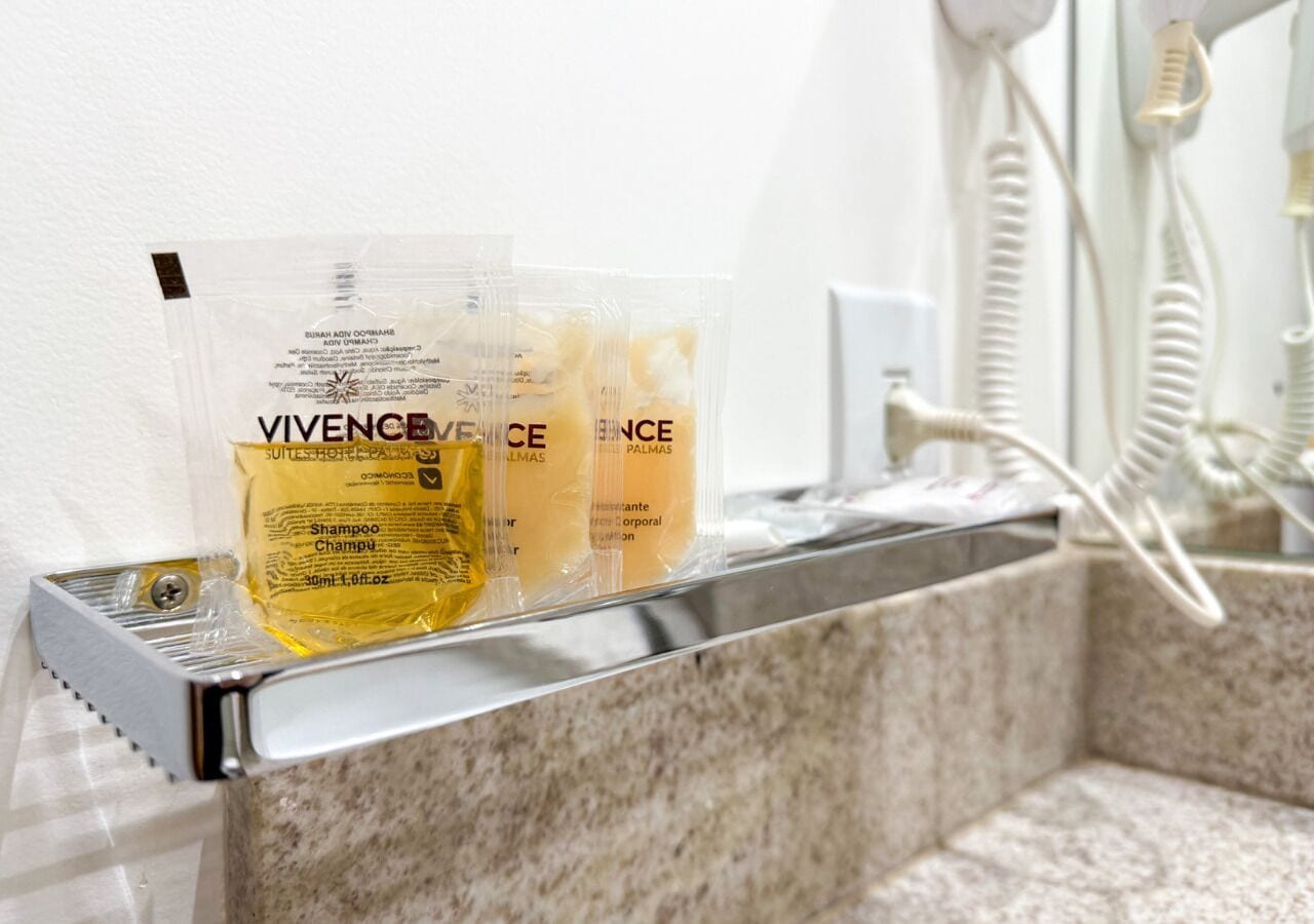 Un baño con lavamanos de mármol, un secador de pelo y tres botellas de champú Vivence sobre el lavamanos.