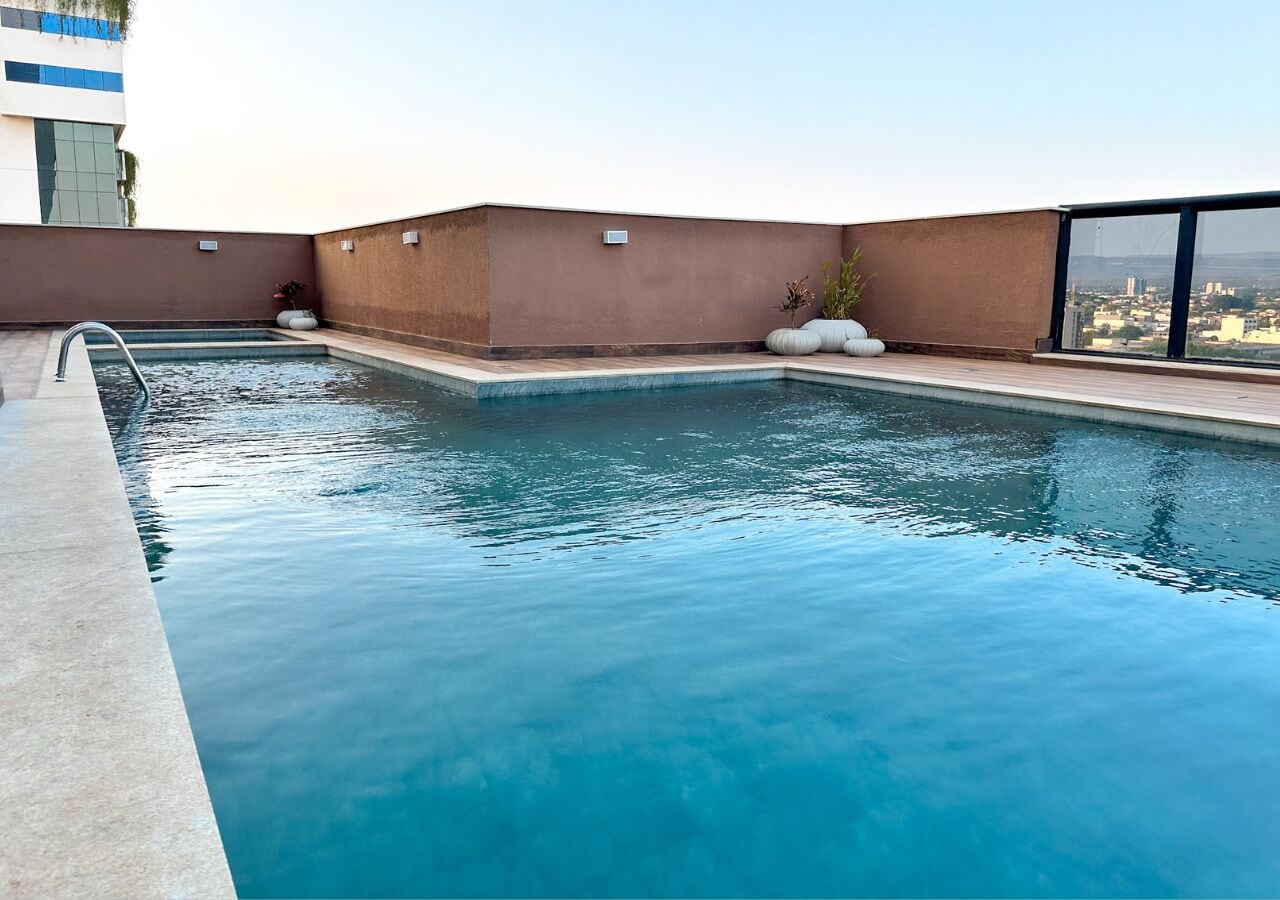 A rooftop pool with clear blue water, surrounded by a low brown wall and a glass railing.