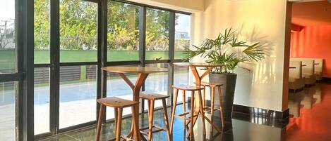 Un moderno vestíbulo de hotel con ventanas amplias, una recepción y una zona de estar con taburetes.
