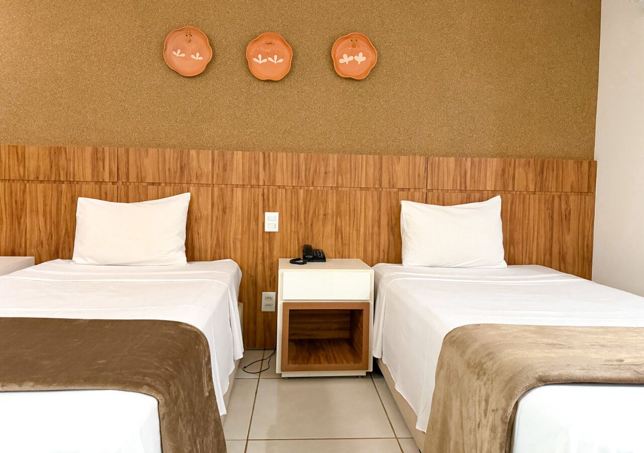 Une chambre d’hôtel avec deux lits, une tête de lit en bois, une table de chevet et trois assiettes décoratives accrochées au mur.