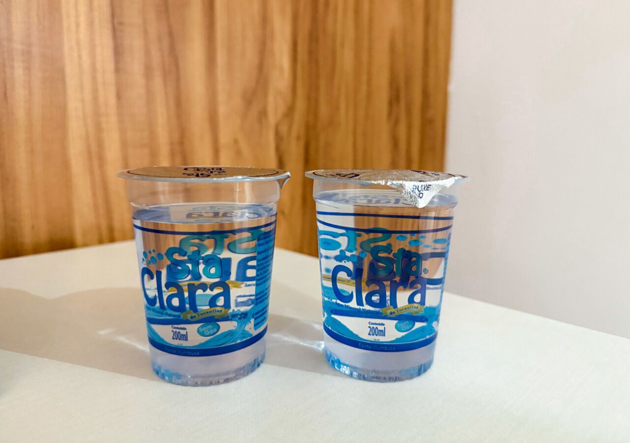 Two clear plastic cups with blue and white labels, placed on a white surface against a wooden background.