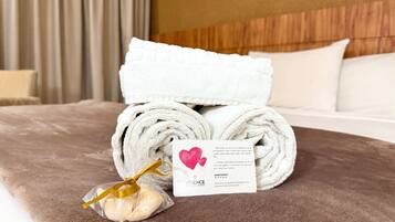 Una cama bien hecha con toallas blancas, una pequeña bolsa de regalo y una tarjeta sobre una colcha marrón.