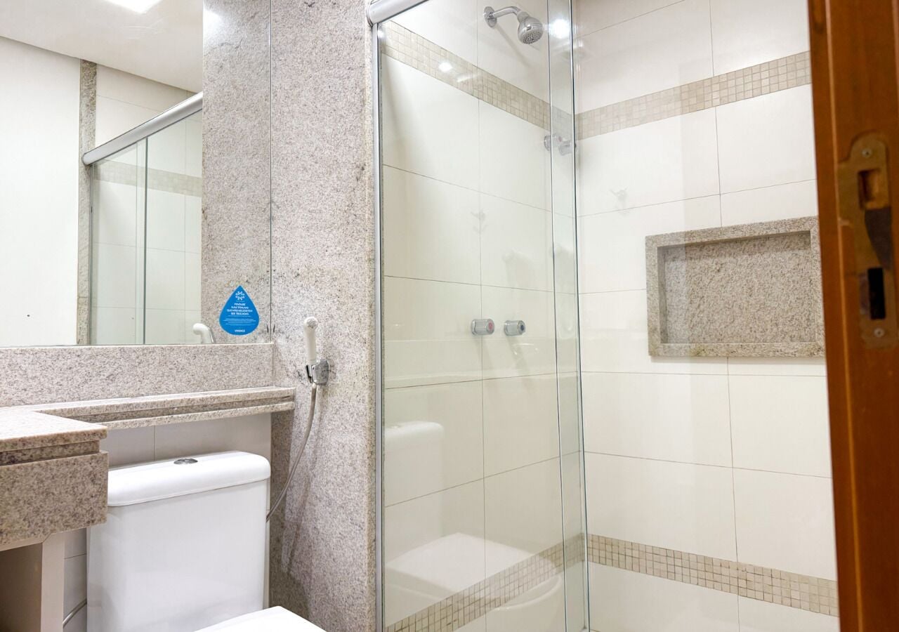 A bathroom with a glass shower enclosure, a white toilet, and a granite countertop.