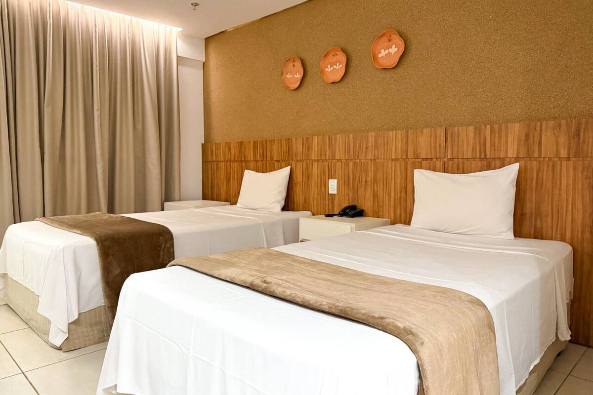 Een hotelkamer met twee bedden, een houten hoofdeinde, een telefoon en een wandlamp.